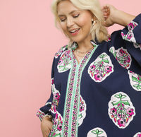 Woman wearing a navy blue top with floral patterns on a light pink background