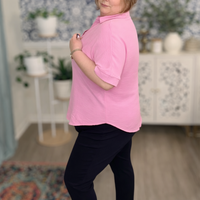 Person wearing a pink shirt and black pants in a room with decorative elements.