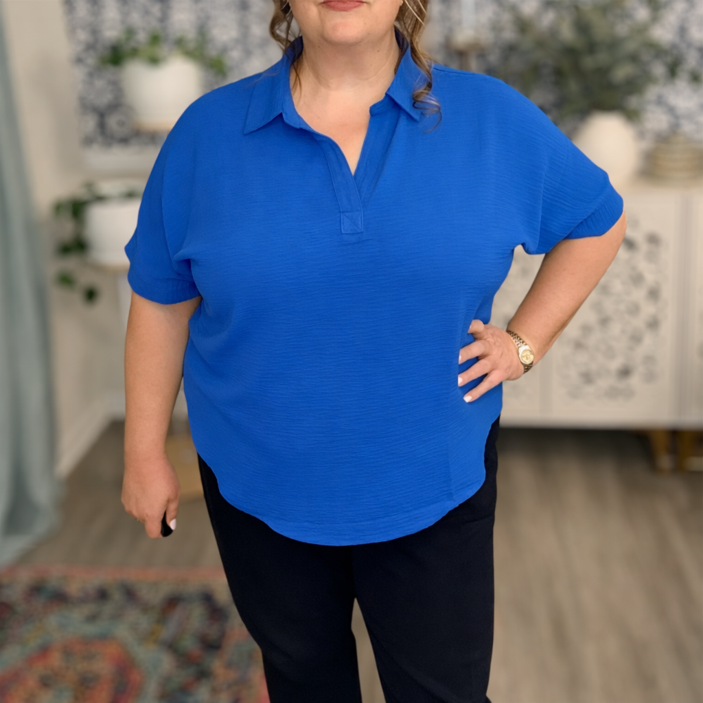 Person wearing a blue polo shirt and black pants indoors.