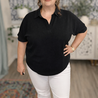 Person wearing a black short-sleeve shirt and white pants in an indoor setting