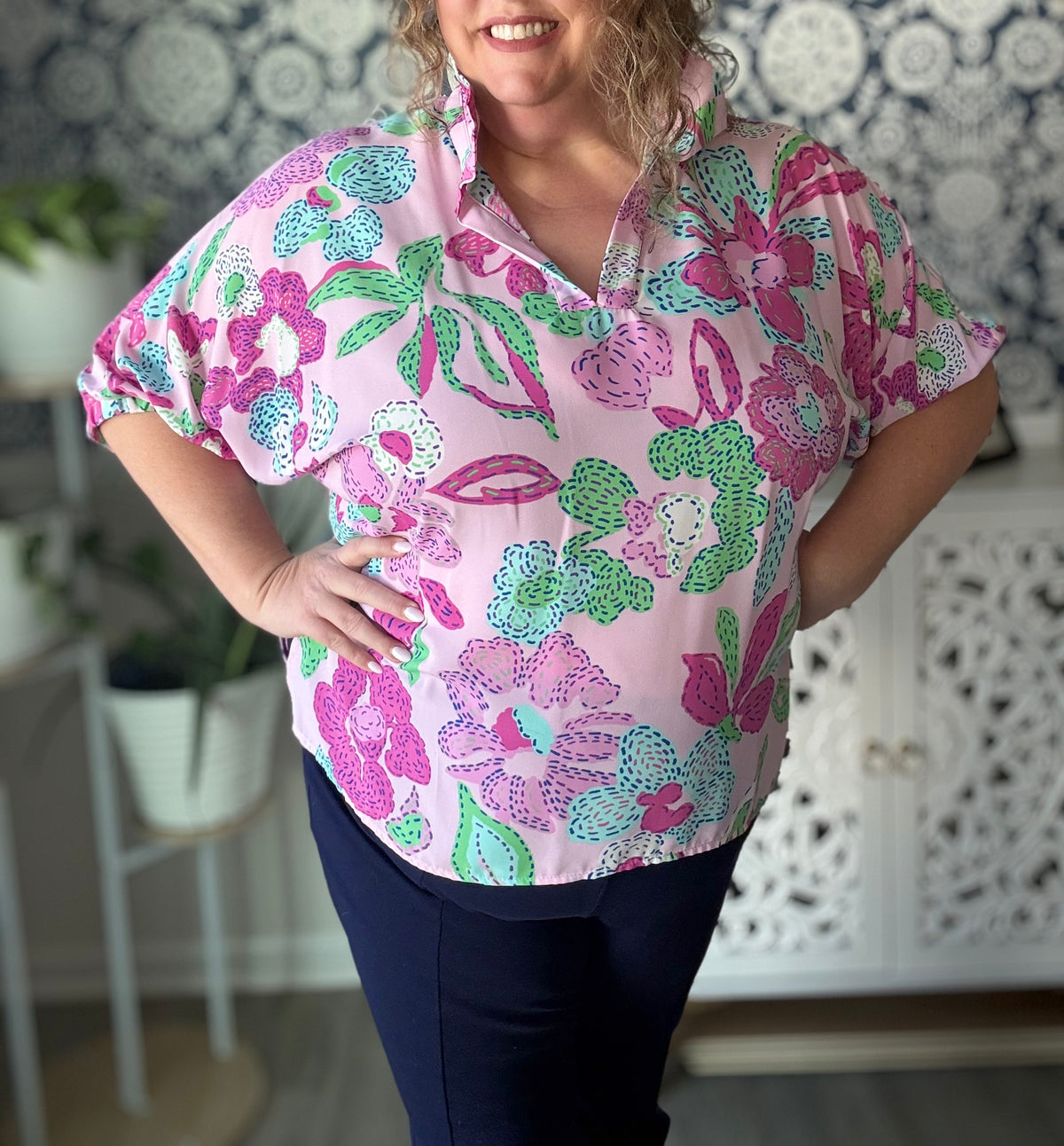 Woman wearing a pink floral blouse in a room with decorative elements.
