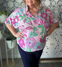 Woman wearing a pink floral blouse in a room with decorative elements.