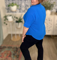 Person wearing a blue shirt and black pants in a room with plants and furniture.